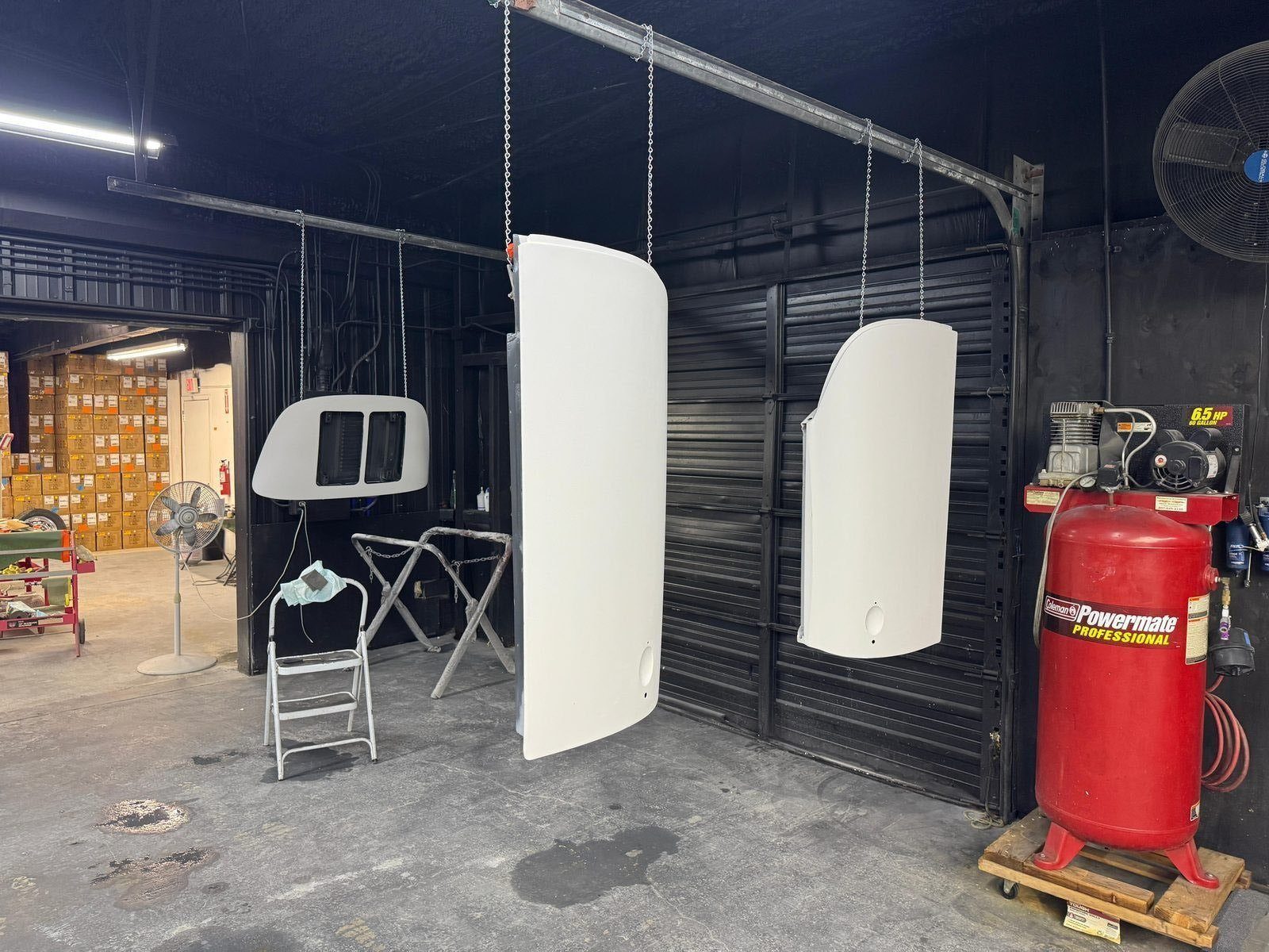 Detached Porsche 356 SC panels hanging from chains in the spray cabin, coated in white primer