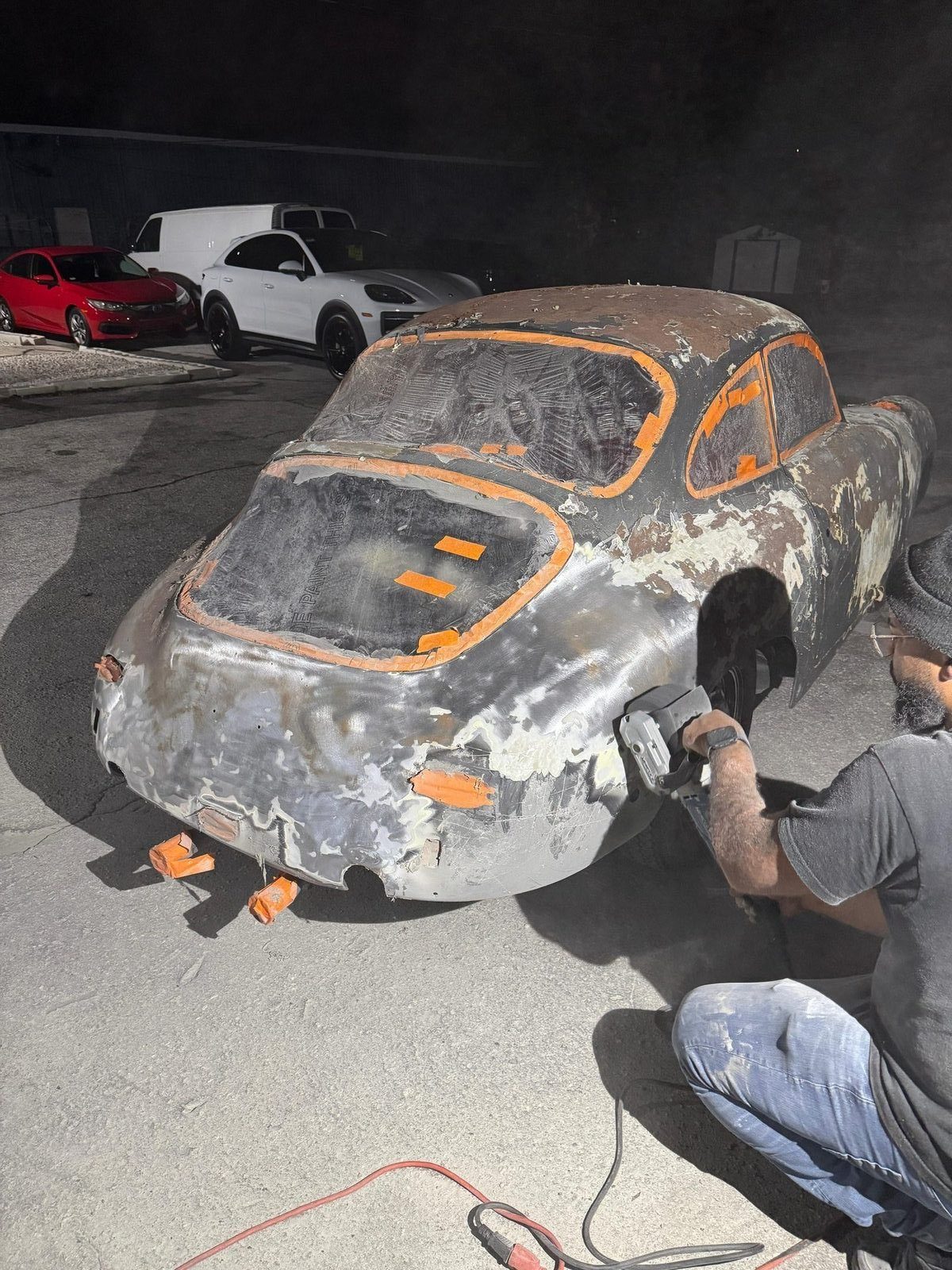 Technician using a power sander to remove paint from the 356 SC body outside the shop